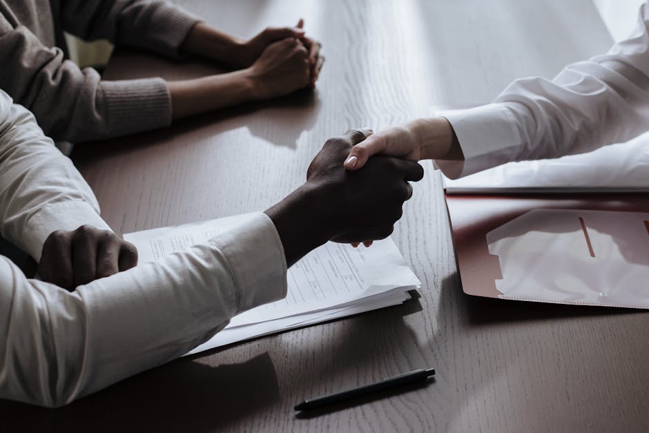 Business agreement with a handshake over contract documents at a meeting table.